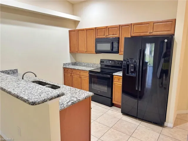 Kitchen featuring black appliances, brown cabinetry, light stone counters, and light tile patterned flooring