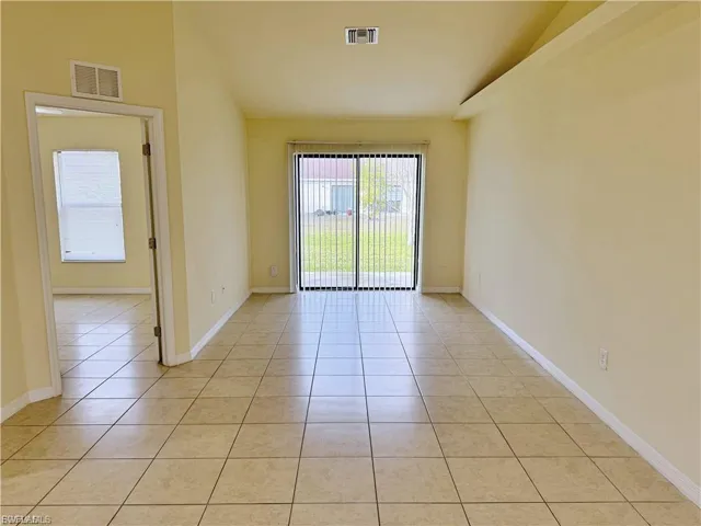 Empty room featuring light tile patterned flooring, plenty of natural light, and vaulted ceiling