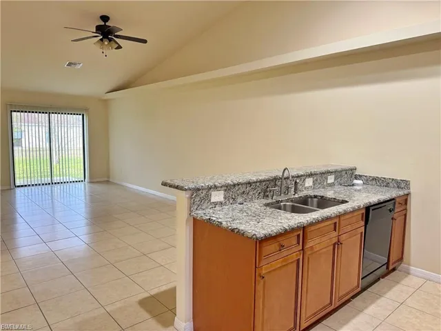 Kitchen with brown cabinets, light stone counters, a peninsula, light tile patterned floors, and open floor plan