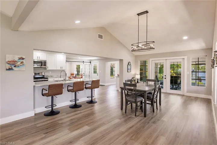 Dining area featuring french doors, LVT wood-type flooring, a notable chandelier, high vaulted ceiling, and sink