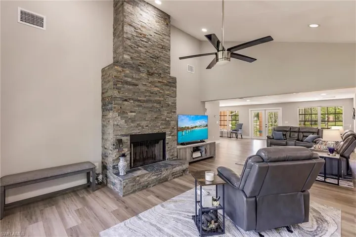 Living room with french doors, a fireplace, light wood-type flooring, high vaulted ceiling, and ceiling fan