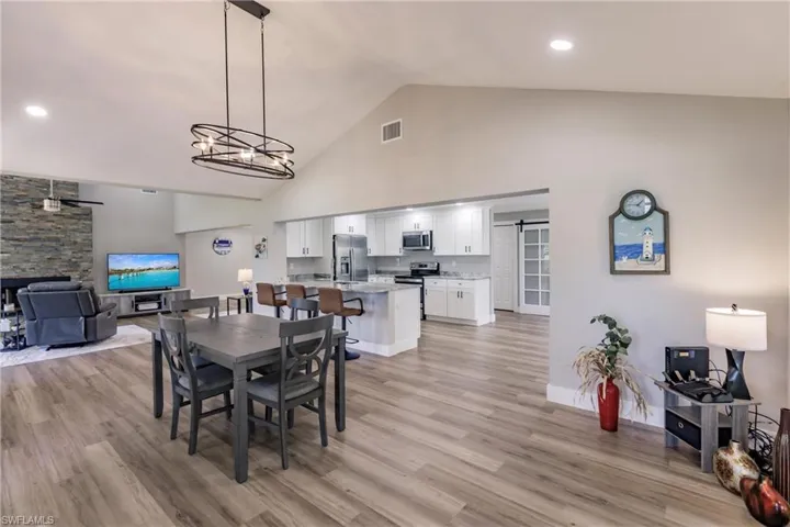 Dining space with a barn door, high vaulted ceiling, light hardwood / wood-style floors, and ceiling fan with notable chandelier