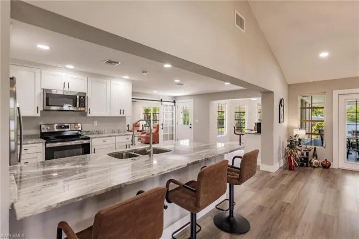 Kitchen featuring LVT wood-type flooring, light stone counters, sink, white cabinetry, and appliances with stainless steel finishes