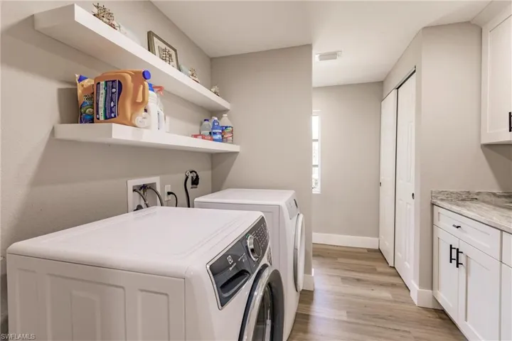 Washroom with cabinets, light, LVT/ wood-style flooring, electric dryer hookup, separate washer and dryer, and hookup for a washing machine