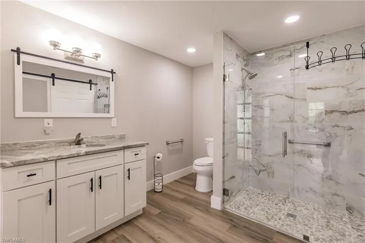 Master Bathroom featuring a shower with shower door, LVT flooring but underneath there is matching tile, toilet, and vanity