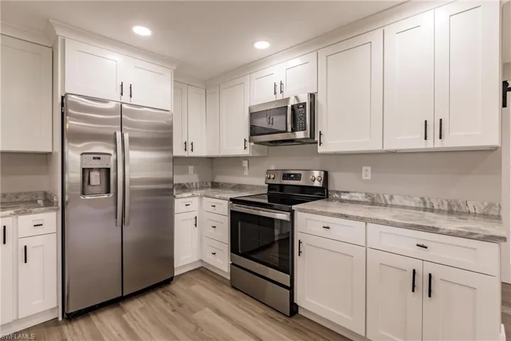 Kitchen with appliances with stainless steel finishes, white cabinets, light stone counters, and light LVT / wood-style flooring