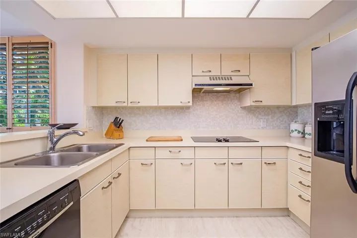 Kitchen featuring a double basin stainless steel sink, light wood-finish cabinetry, a built-in electric cooktop, and a mosaic tile backsplash