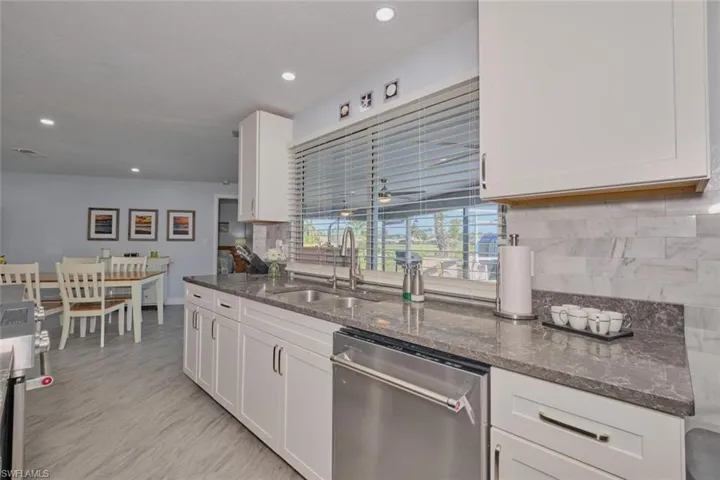 Kitchen with sink, dishwasher, white cabinetry, and dark stone countertops