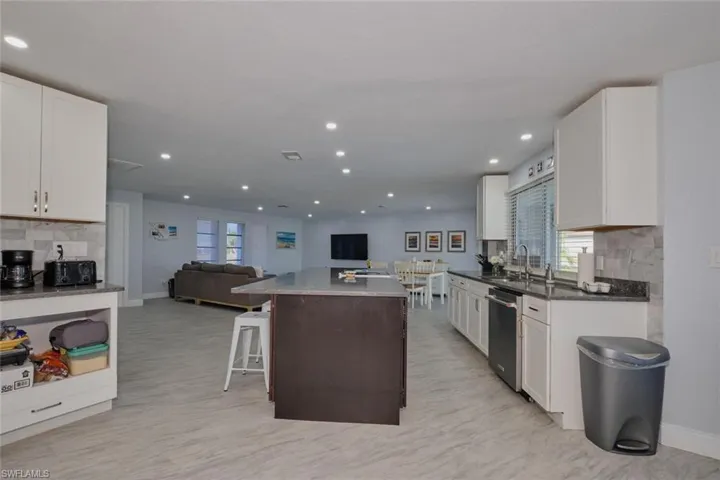 Kitchen with white cabinetry, decorative backsplash, stainless steel dishwasher, and a kitchen breakfast bar