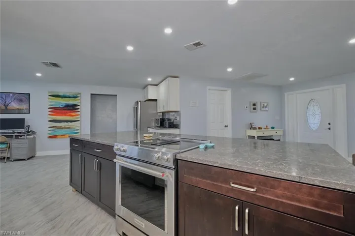 Kitchen featuring white cabinets, light stone countertops, stainless steel appliances, and dark brown cabinets