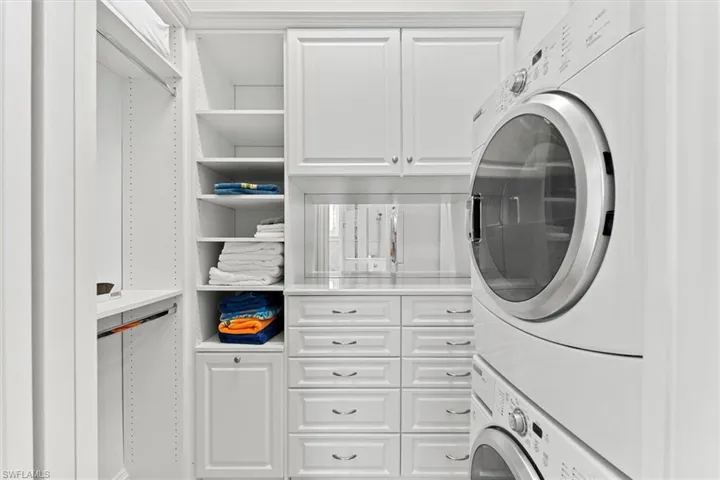 Clothes washing area featuring stacked washer and dryer and cabinets