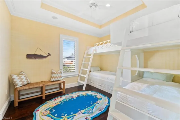 Bedroom featuring a raised ceiling, ornamental molding, hardwood / wood-style flooring, and ceiling fan