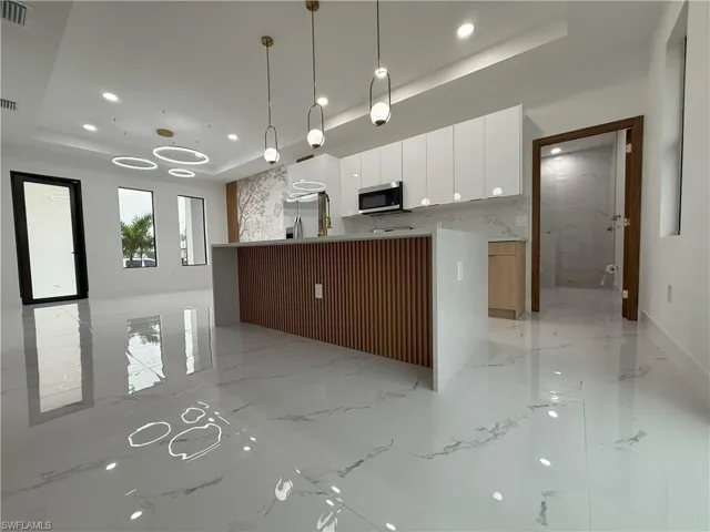 Kitchen featuring white cabinets, a tray ceiling, modern cabinets, hanging light fixtures, and appliances with stainless steel finishes
