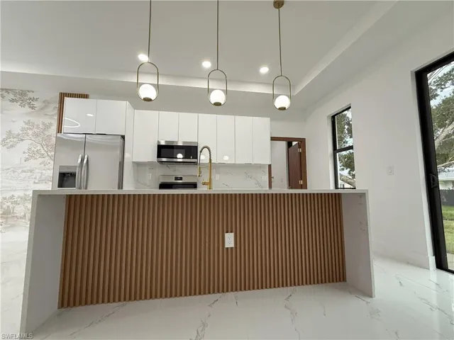 Kitchen with light marble finish floors, white cabinets, appliances with stainless steel finishes, light stone countertops, and modern cabinets