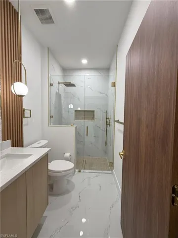 Bathroom with vanity, a marble finish shower, light marble finish flooring, and recessed lighting