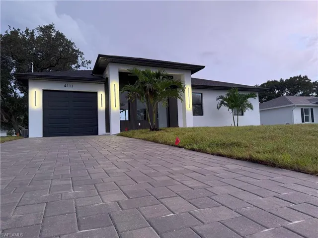 View of front of property featuring a garage, stucco siding, decorative driveway, and a front lawn