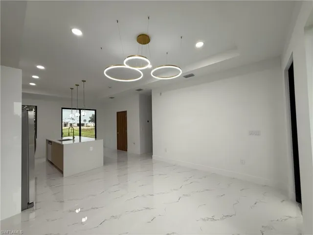 Empty room featuring a chandelier, recessed lighting, light marble finish floors, and a raised ceiling