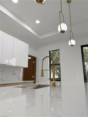 Kitchen featuring modern cabinets, white cabinets, light stone counters, pendant lighting, and a tray ceiling