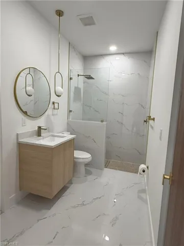 Full bath featuring vanity, a marble finish shower, light marble finish floors, and recessed lighting