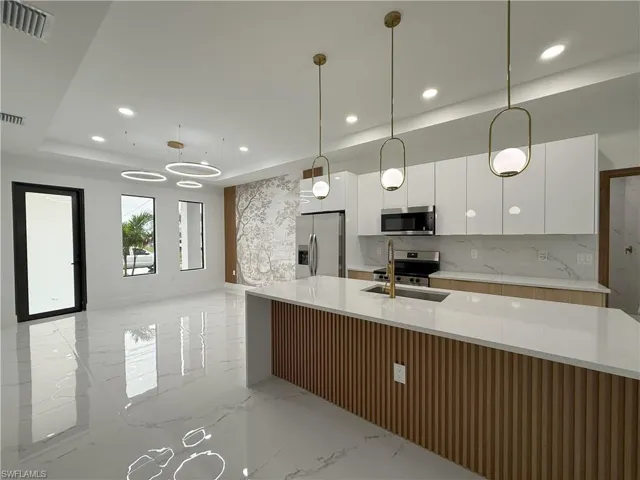 Kitchen featuring white cabinetry, stainless steel appliances, hanging light fixtures, light stone counters, and light marble finish flooring