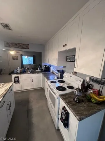 Kitchen featuring stove, white cabinetry, finished concrete flooring, dark countertops, and a peninsula