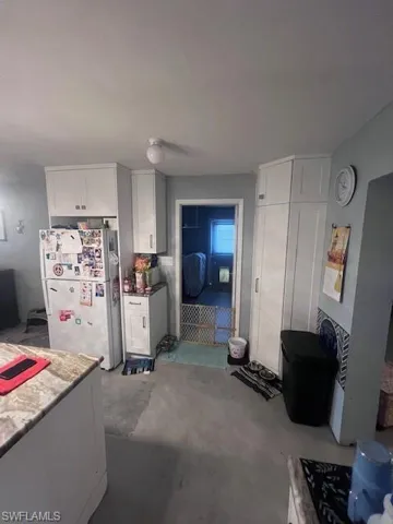 Kitchen with white cabinets, refrigerator, and unfinished concrete floors