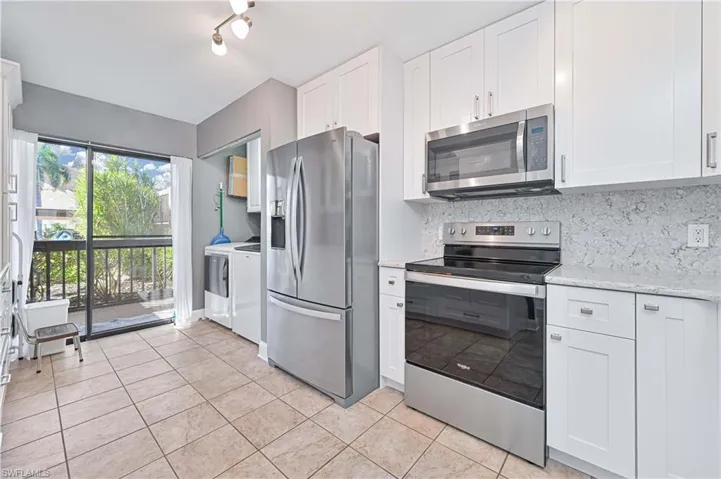 Kitchen featuring appliances with stainless steel finishes, white cabinets, tasteful backsplash, and light stone counters