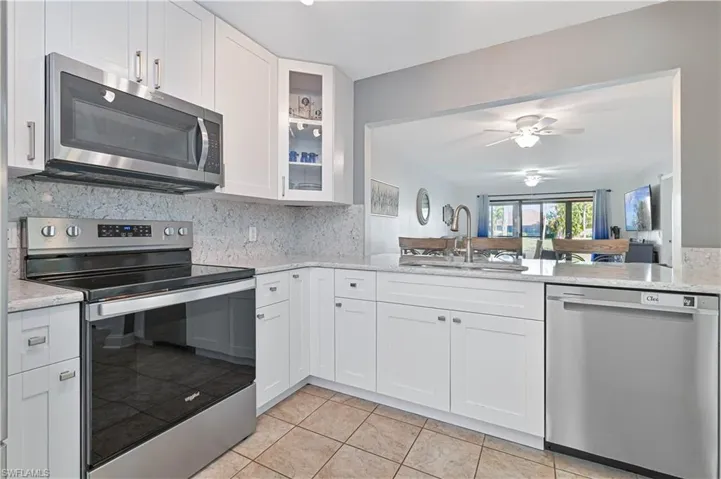 Kitchen with appliances with stainless steel finishes, glass insert cabinets, light stone countertops, and white cabinetry