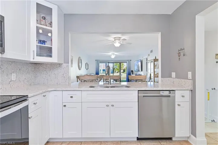 Kitchen with white cabinets, light stone counters, stainless steel appliances, and glass insert cabinets