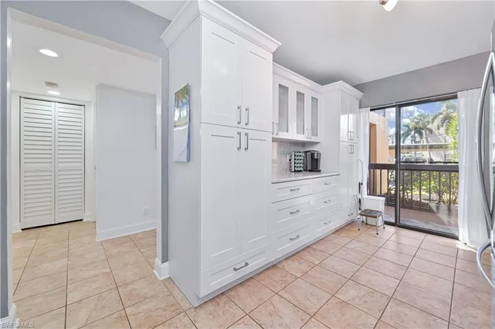 Kitchen featuring glass insert cabinets, white cabinetry, light tile patterned floors, and freestanding refrigerator
