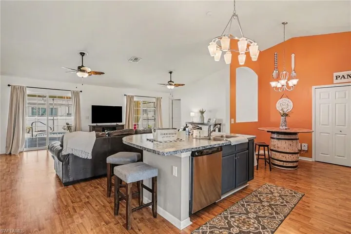 Kitchen featuring open floor plan, dishwasher, a center island with sink, light wood-type flooring, and vaulted ceiling