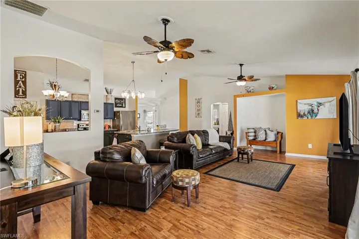 Living room featuring suspended lighting, wood finished floors, vaulted ceiling, ceiling fan, and arched walkways
