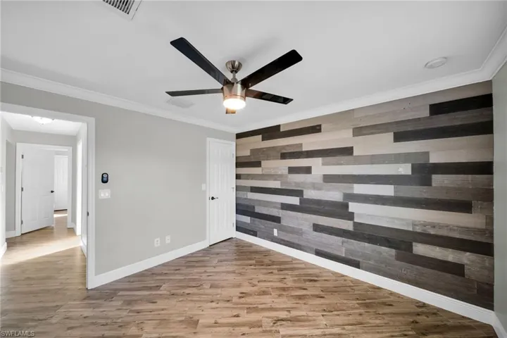 Empty room with an accent wall, ceiling fan, wood finished floors, baseboards, and ornamental molding