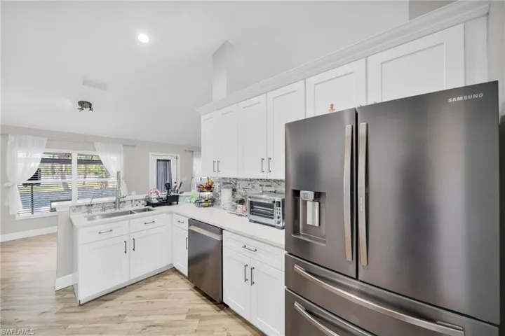 Kitchen with appliances with stainless steel finishes, a sink, white cabinets, light countertops, and a peninsula
