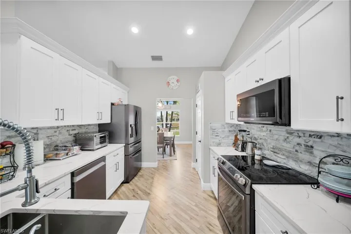 Kitchen with stainless steel appliances, white cabinetry, backsplash, and recessed lighting