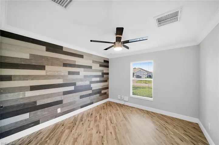 Empty room with wooden walls, baseboards, crown molding, wood finished floors, and an accent wall