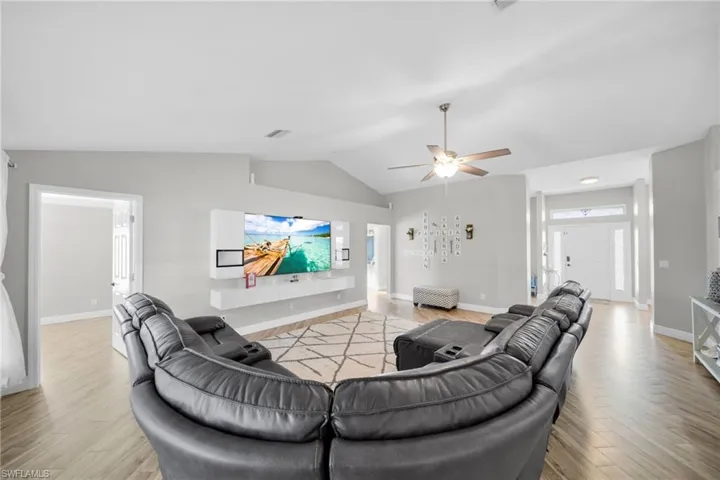Living area with lofted ceiling, lig)ht wood-type flooring, baseboards, and ceiling fan