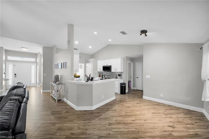 Kitchen featuring stainless steel microwave, open floor plan, white cabinets, light wood finished floors, and lofted ceiling