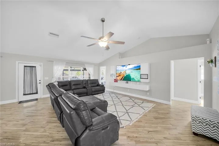Living room featuring lofted ceiling, ceiling fan, light wood-type flooring, and baseboards