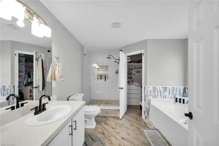 Bathroom featuring wood finished floors, a shower stall, a garden tub, vanity, and a walk in closet