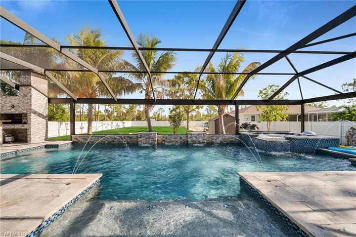 View of swimming pool featuring an outdoor stone fireplace, a patio, a fenced backyard, and a pool with connected hot tub