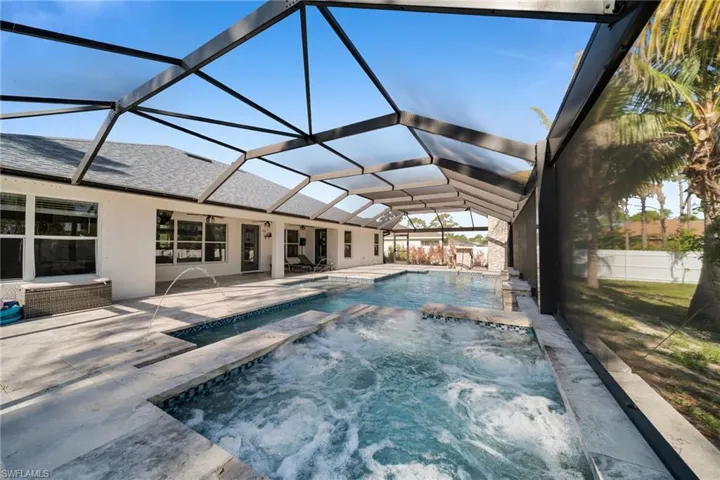 View of pool featuring a patio, glass enclosure, and a pool with connected hot tub
