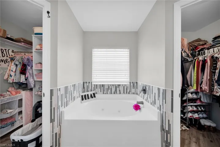 Full bath with a jetted tub, a walk in closet, and wood finished floors