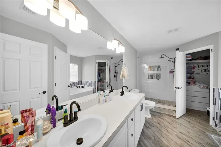 Bathroom with a stall shower, wood finishe'd floors, double vanity, toilet, and a spacious closet
