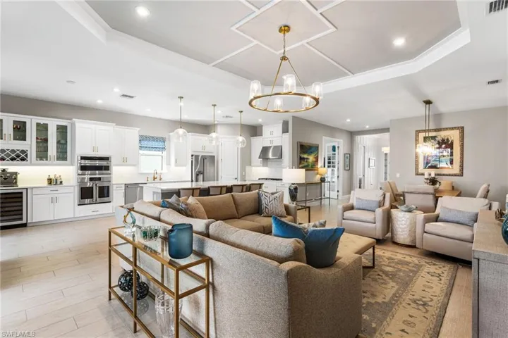 Living area with hanging lights, wine cooler, light wood-style flooring, and a tray ceiling