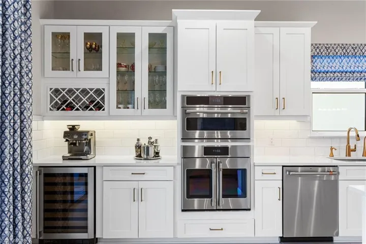 Kitchen featuring white cabinetry, stainless steel appliances, beverage cooler, and light stone countertops