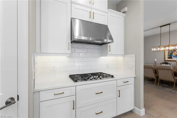 Kitchen with white cabinets, decorative backsplash, light stone countertops, and light wood finished floors