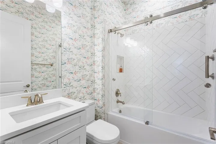 Full bath featuring wallpapered walls, combined bath / shower with glass door, and vanity