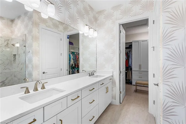 Bathroom with a spacious closet, wallpapered walls, double vanity, and a marble finish shower