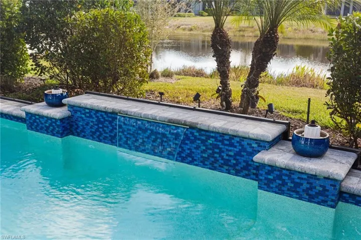Outdoor pool with a water view, a patio, and a lawn